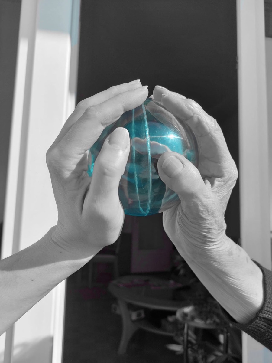 Mains d'une personne âgée et d'un accompagnant autour d'une balle, symbole de soutien et de lien